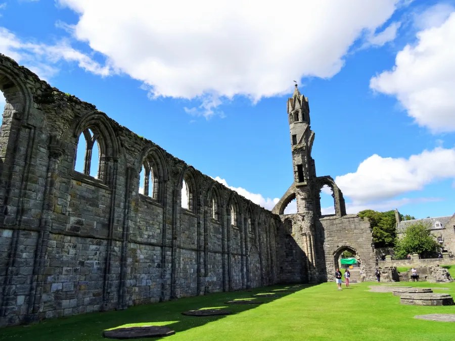 Ruinen der Kathedrale von St. Andrews mit blauem Himmel und grünem Rasen, Menschen erkunden die Umgebung.