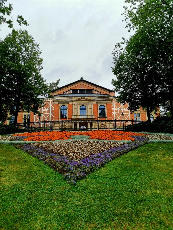 Das Bayreuther Festspielhaus, umgeben von bunten Blumenbeeten und Bäumen.
