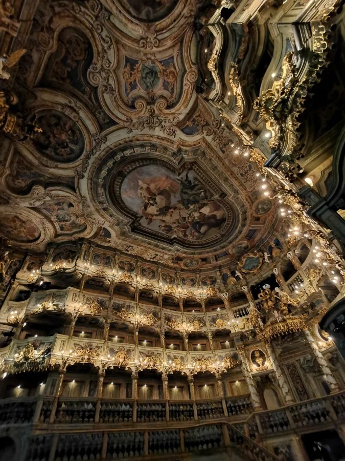 Detailaufnahme des prunkvollen Inneren des Markgräflichen Opernhauses mit kunstvollen Deckenmalereien, reich verzierten Balkonen und goldenen Ornamenten.