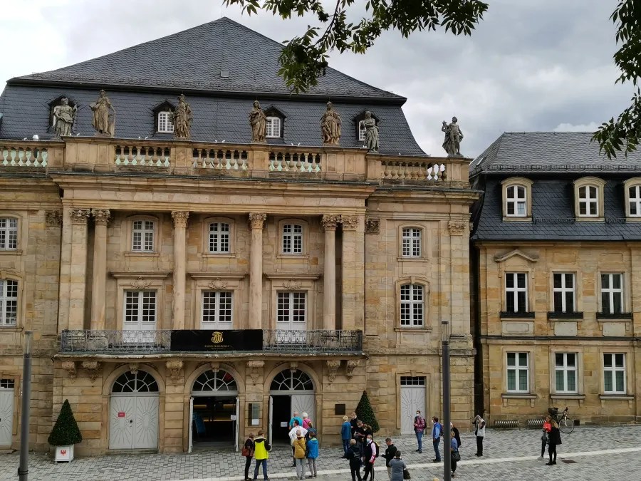 Historische Architektur eines Gebäudes mit Statue auf dem Dach, umgeben von Besuchern und Bäumen.