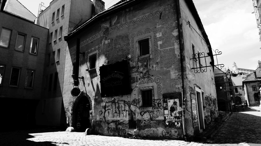 Ein historisches Gebäude mit bunter Graffiti-Kunst, umgeben von modernen Gebäuden in einer Stadtstraße in Schwarz-Weiß.