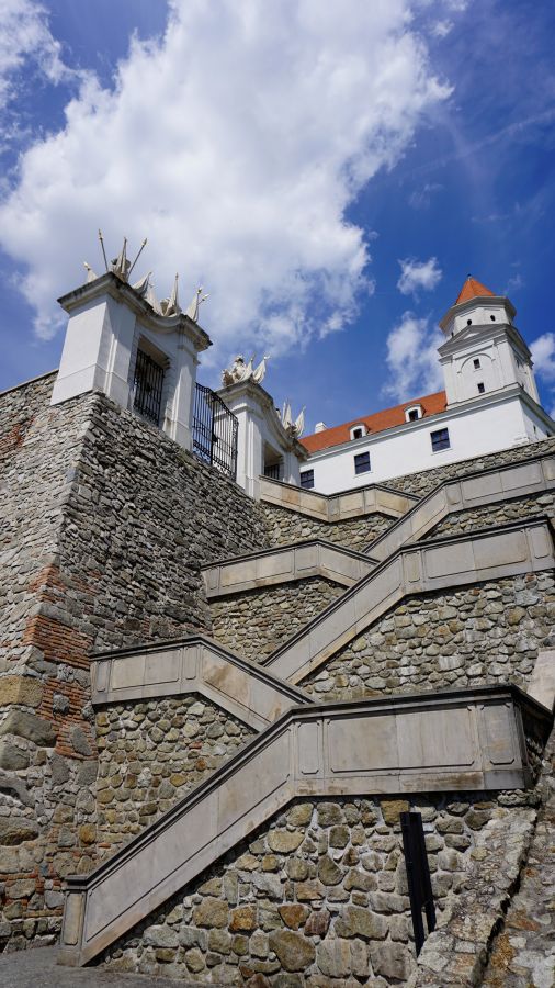 Blick auf die Burg Bratislava, die sich über steinerne Treppen mit einem klaren blauen Himmel im Hintergrund erhebt.