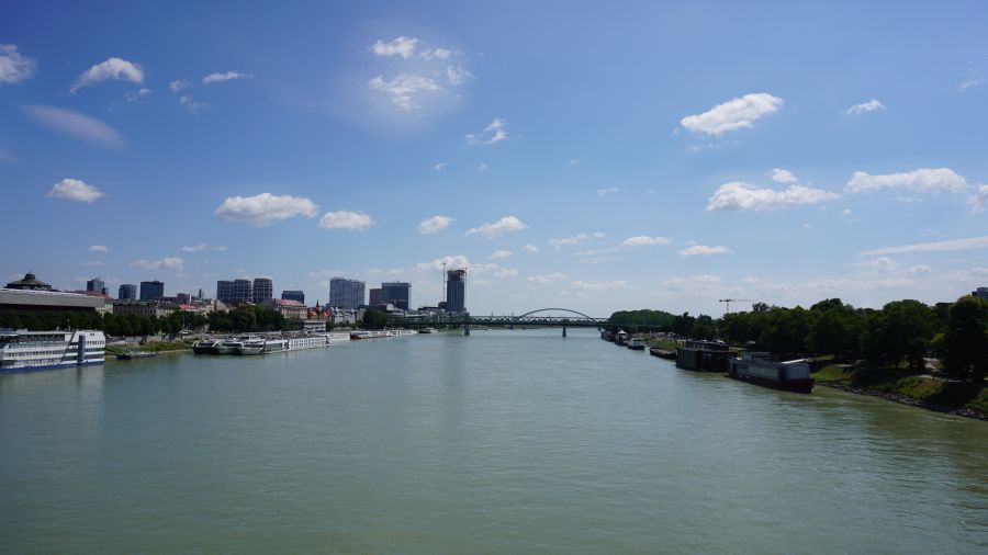 Blick auf die Donau mit Schiffen und der Stadt Bratislava im Hintergrund unter blauem Himmel.
