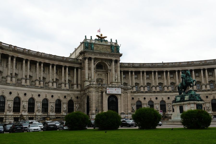 Blick auf die Hofburg in Wien mit einer Statue und grünen Hecken im Vordergrund.