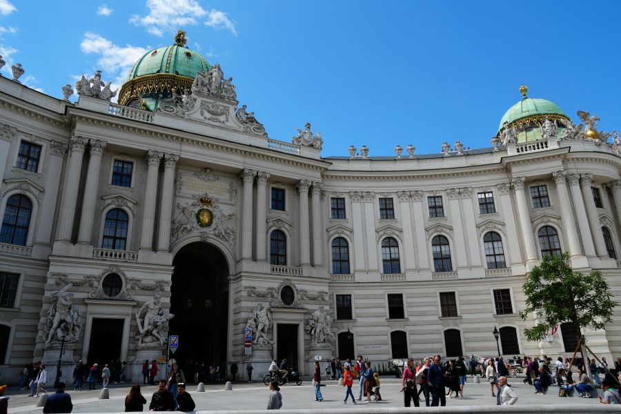 Der Eingang zur Hofburg mit beeindruckender Architektur und Menschen, die vorbeigehen, unter einem klaren blauen Himmel.