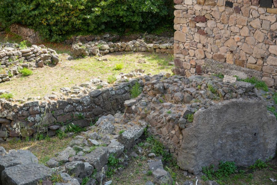 Ruinen einer alten Steinstruktur in einem grünen Umfeld, mit sichtbaren Steinen und Pflanzen im Hintergrund.