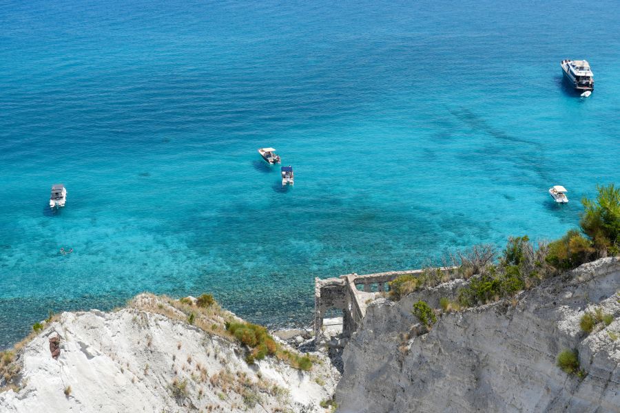 Ein Blick auf das glasklare Wasser vor der Küste mit mehreren Booten und einem alten, verblichenen Bauwerk auf einer Klippe.