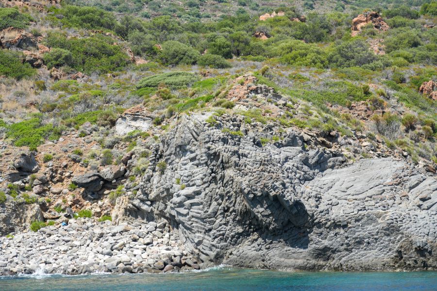 Felsige Küstenlandschaft mit grüner Vegetation und klarem Wasser im Vordergrund.
