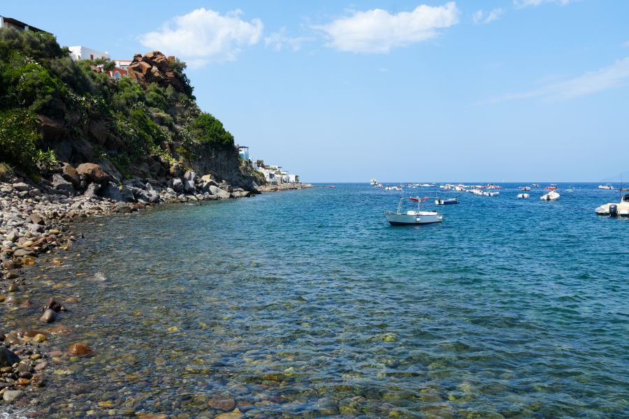 Blick auf die Küste von Panarea mit Wasser, Steinen und kleinen Booten im Hafen.