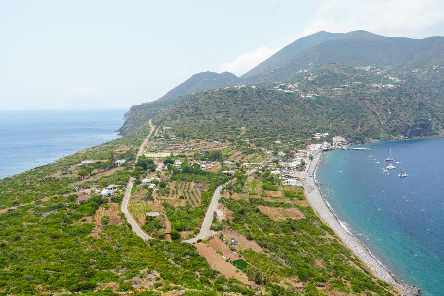 Landschaftsaufnahme der Liparischen Inseln mit grünen Hügeln, weißen Häusern und dem blauen Meer im Vordergrund.