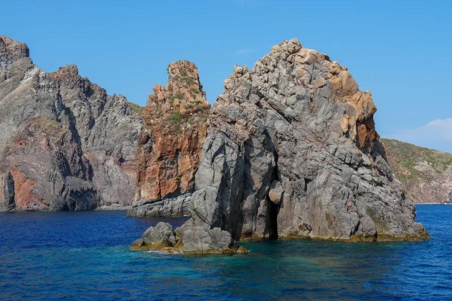 Felsenformation im klaren blauen Wasser des Mittelmeers, umgeben von steilen Klippen und einer blauen Himmel im Hintergrund.