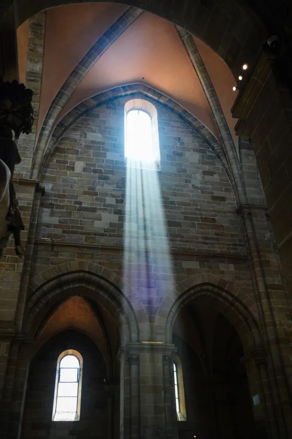 Lichtstrahlen durch ein Fenster in einem historischen Gebäudeeingang mit Steinmauern und gotischen Bögen.