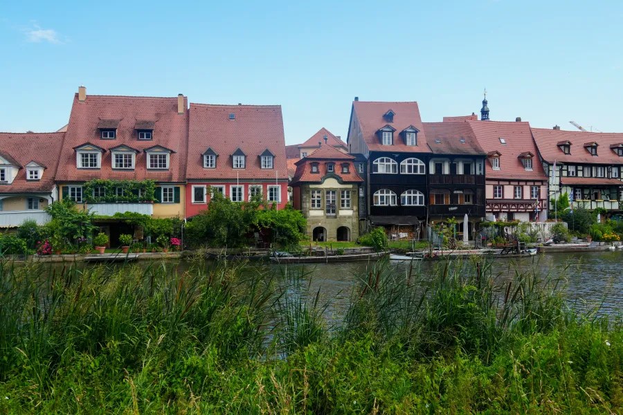 Fachwerkhäuser am Ufer der Regnitz in Bamberg, umgeben von üppigem Grün.