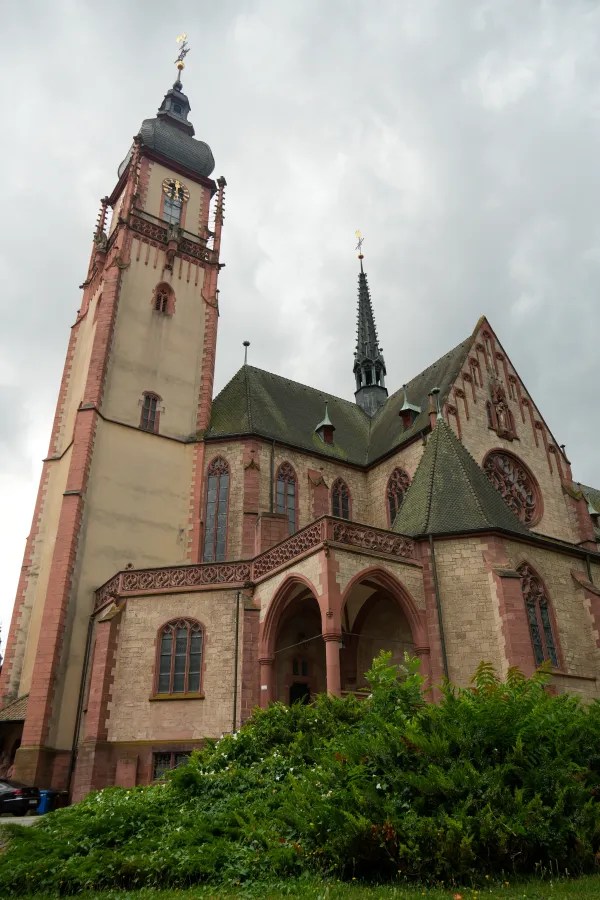 View of a historic church building with intricate architectural details, featuring a tall tower and pointed spires against a cloudy sky.