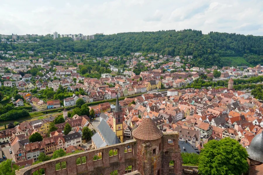 Panoramic view of a town with colorful houses nestled among green hills, featuring a historic castle or fortification in the foreground.
