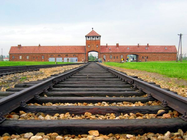 Blick auf die Gleise, die zum Eingang des ehemaligen Konzentrationslagers Auschwitz-Birkenau führen, mit dem Wachturm im Hintergrund.