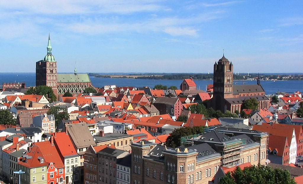 Blick auf die Altstadt von Stralsund mit roten Dächern und historischen Kirchen, im Hintergrund der Bodden.