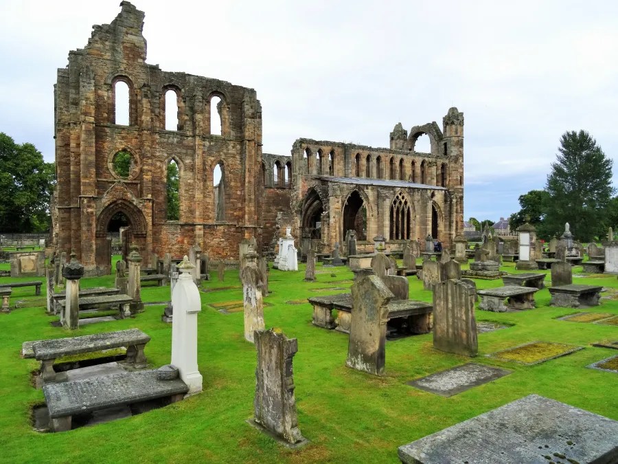 Ruinen einer alten Kathedrale umgeben von historischen Grabsteinen auf grünem Rasen.