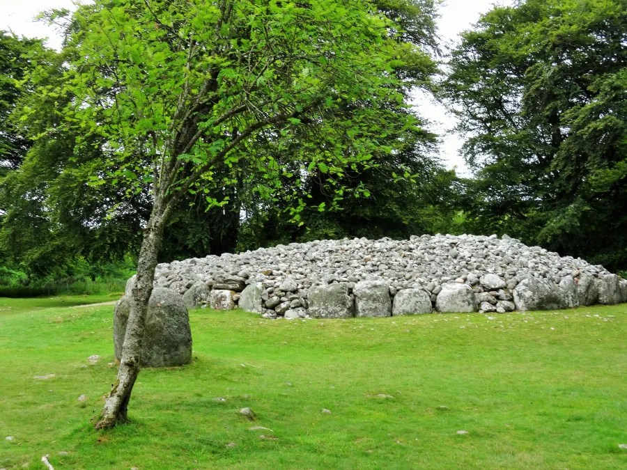 Steingrab aus der Bronzezeit, umgeben von Bäumen und grünem Gras, in der Nähe von Clava Cairns, Schottland.
