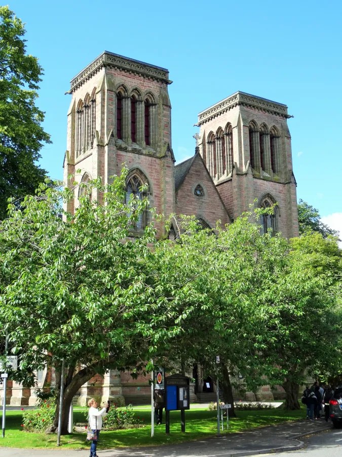 Die St. Andrew's Cathedral in Inverness, umgeben von Bäumen und blauem Himmel, zeigt eine beeindruckende Architektur mit zwei Türmen.