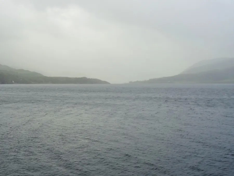 Blick auf einen nebligen See umgeben von sanften Hügeln in Schottland, die Atmosphäre ist ruhig und mystisch.