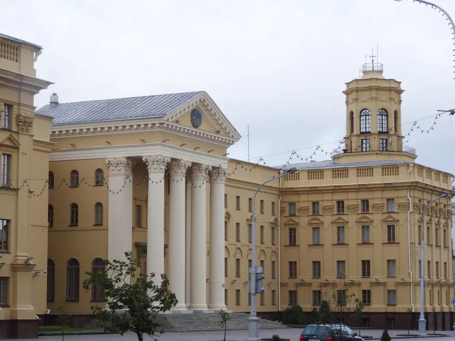 Die Fassade eines historischen Gebäudes in Minsk mit Säulen und einer markanten Uhr, umgeben von weiteren architektonisch ansprechenden Strukturen.