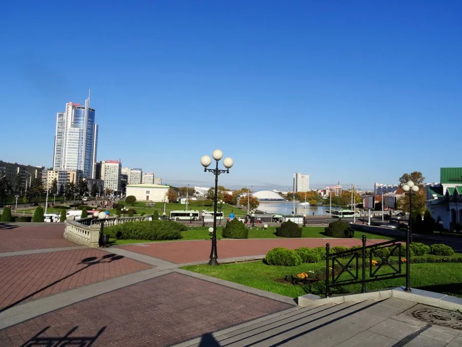 Blick auf einen Stadtpark mit modernen Gebäuden im Hintergrund, klarer blauer Himmel und herbstliche Bäume im Vordergrund.
