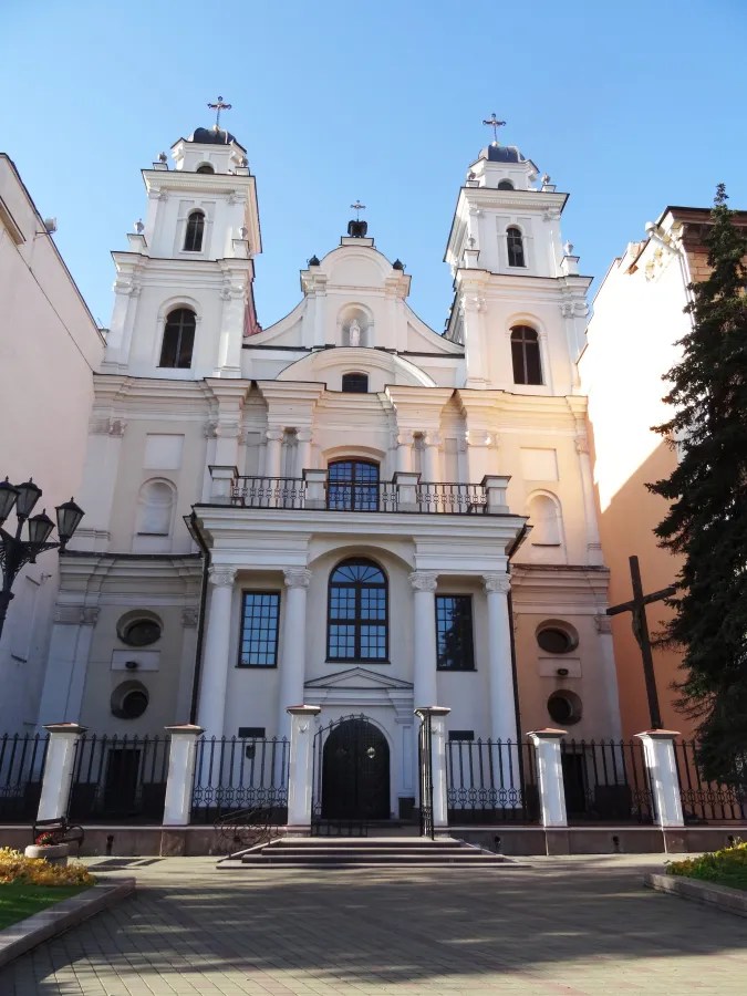 Die Fassade einer orthodoxen Kirche in Minsk, weiß und schlicht, mit zwei Türmen und einem Kreuz, vor einem blauen Himmel.