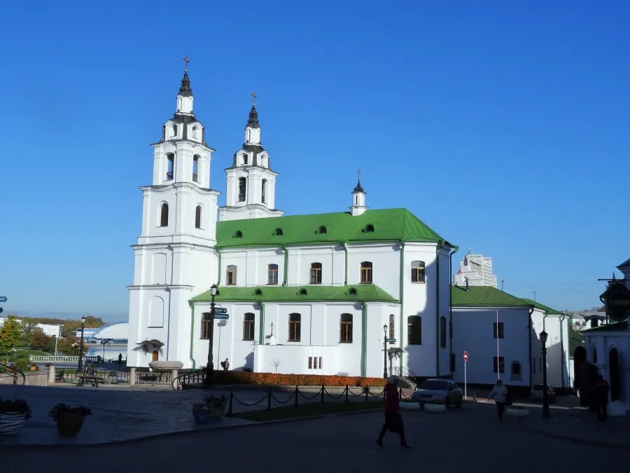 Blick auf eine weiße Kirche mit grünen Dächern und zwei Türmen vor blauem Himmel in Minsk.