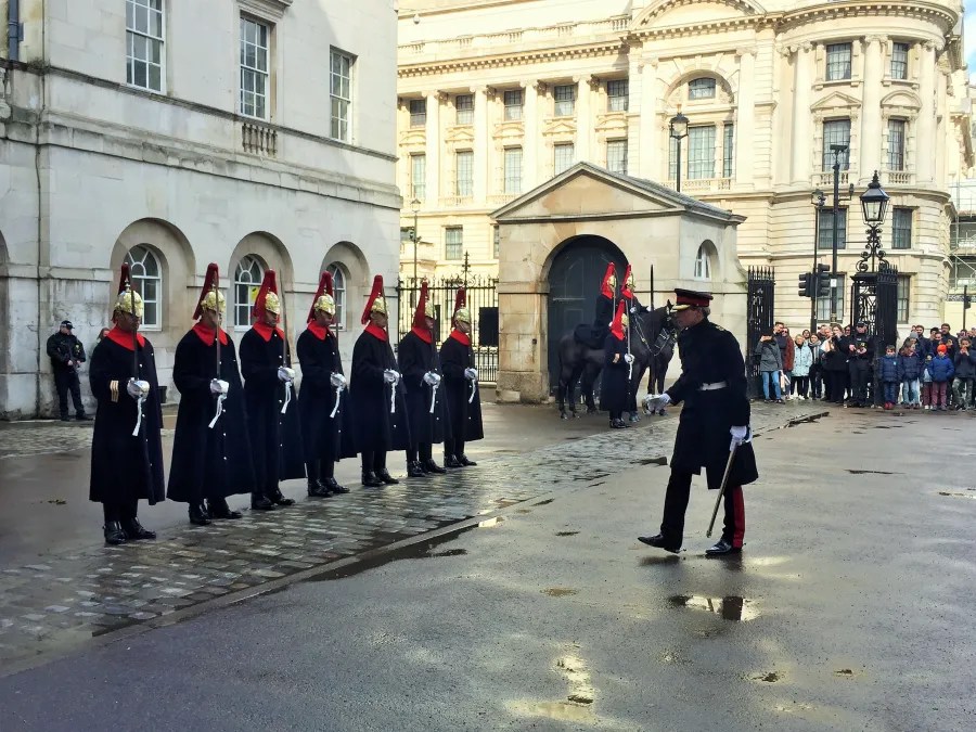 Soldaten in traditioneller Uniform führen eine Wachablösung in London durch, während eine Menschenmenge zuschaut.