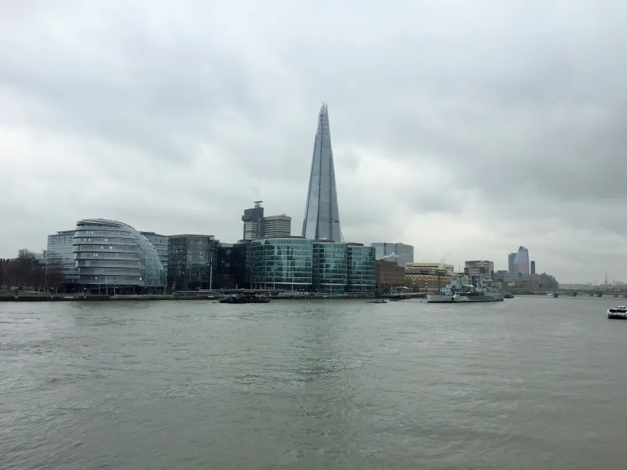 Blick auf die Themse mit dem hohen Shard-Gebäude im Hintergrund und modernen Glasbauten auf der linken Seite, alles unter einem grauen Himmel.