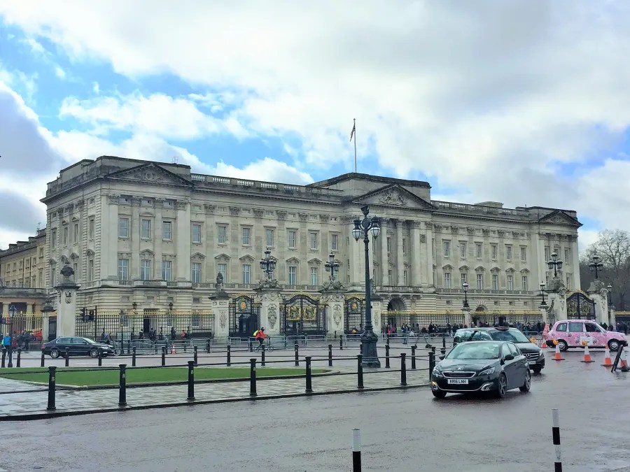 Buckingham Palace in London, featuring its iconic architecture and flag atop the building, with a cloudy sky in the background.