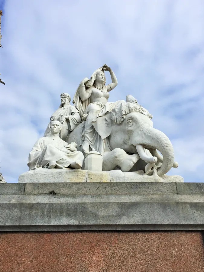 Skulpturengruppe mit einer Darstellung von Britannia auf einem Elefanten, umgeben von weiteren Figuren, vor einem wolkenverhangenen Himmel.