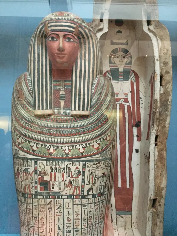 Eine ägyptische Mumie in einem kunstvoll dekorierten Sarkophag, gezeigt in einem Museum. Die Mumie trägt traditionelle Grabkleidung mit reichhaltigen Farben und Hieroglyphen.