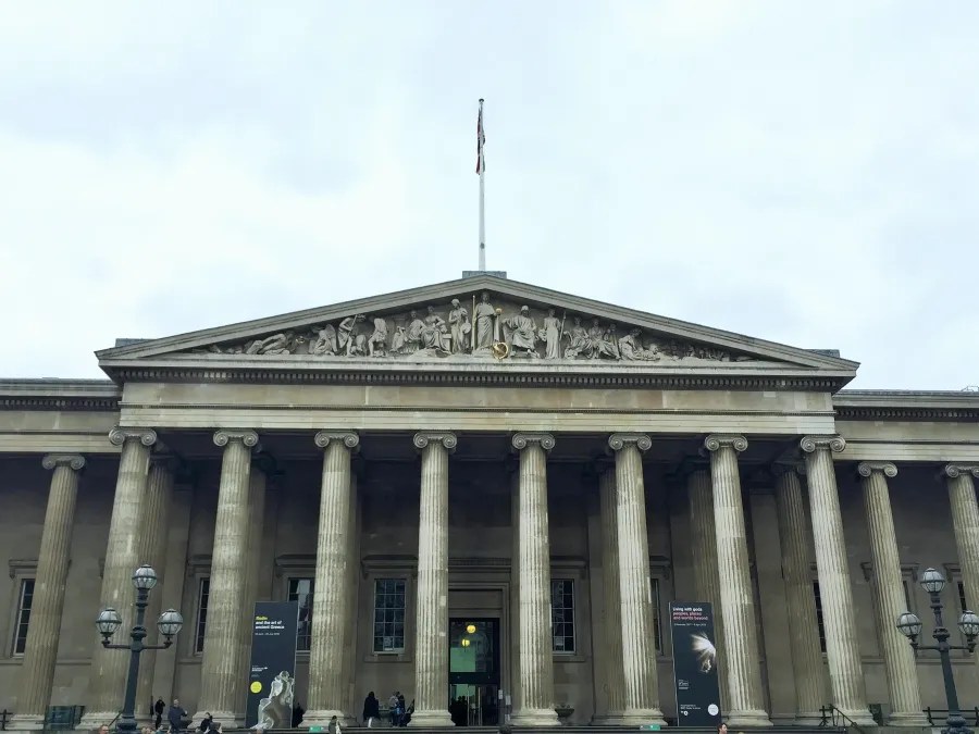 Fassade des British Museum in London, mit Säulen und kunstvollen Skulpturen, unter einem grauen Himmel.