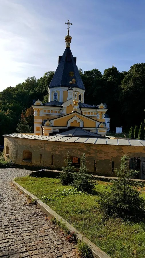 Ein farbenfrohes orthodoxes Kloster mit goldenen Kuppeln, umgeben von Bäumen und Grünflächen, aufgenommen an einem klaren Tag.