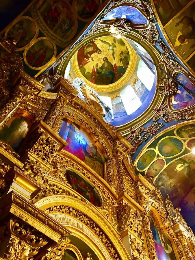 Innenansicht einer prunkvollen orthodoxen Kirche mit goldverzierten Ikonen und bunten Fresken an der Decke.
