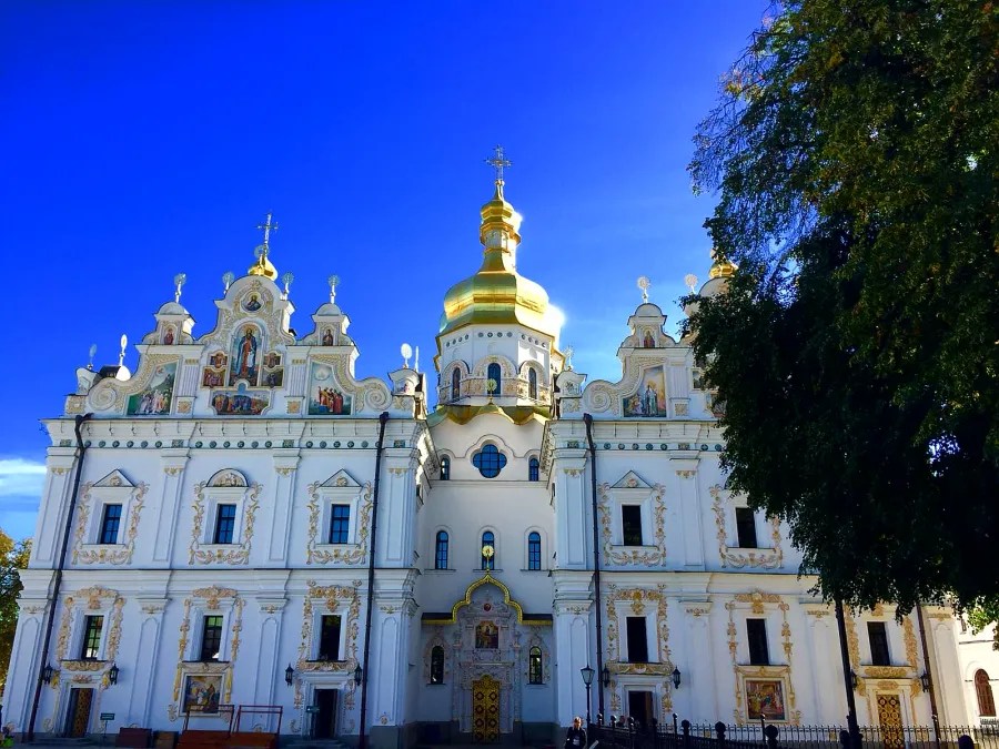 Blick auf die prunkvolle Architektur eines Klosters mit goldenen Kuppeln und bunten Fresken unter einem strahlend blauen Himmel.