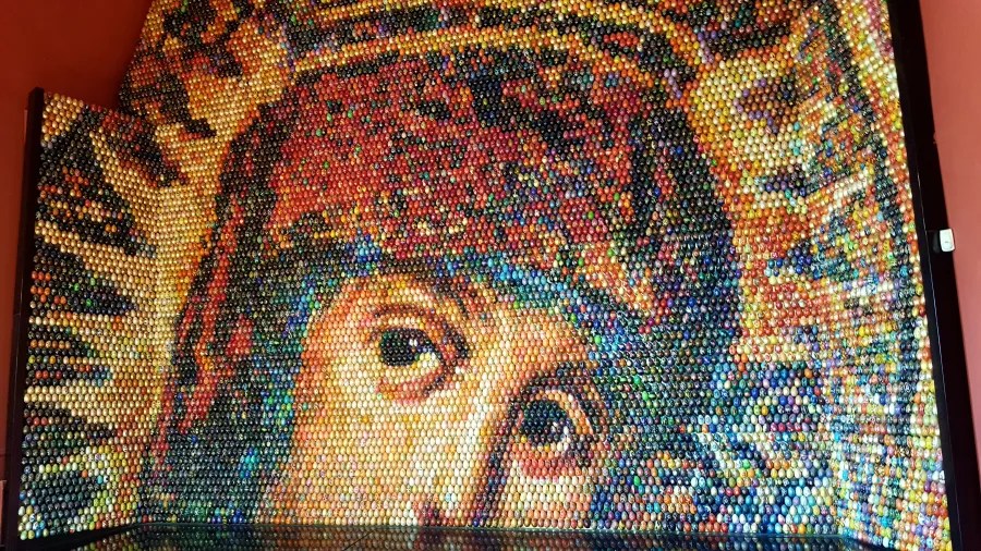 Kunstwerk aus zahlreichen bunten Kappen, das eine ikonische Figur darstellt.