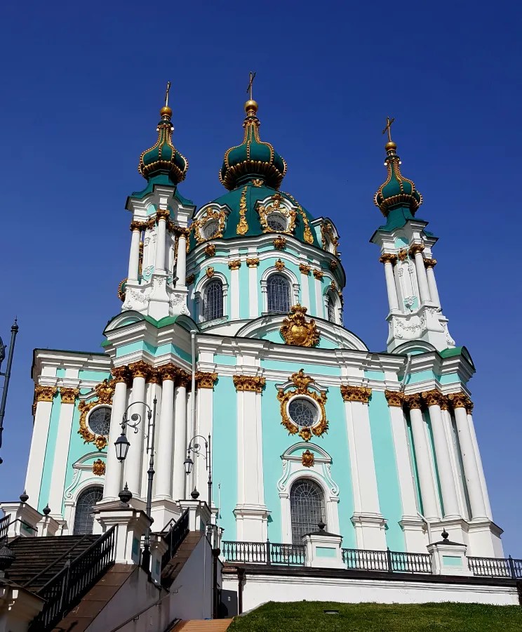 Die St.-Andreas-Kirche in Kiew, eine prunkvolle Barockkirche mit einer blauen Fassade und goldenen Verzierungen, steht unter klarem Himmel.