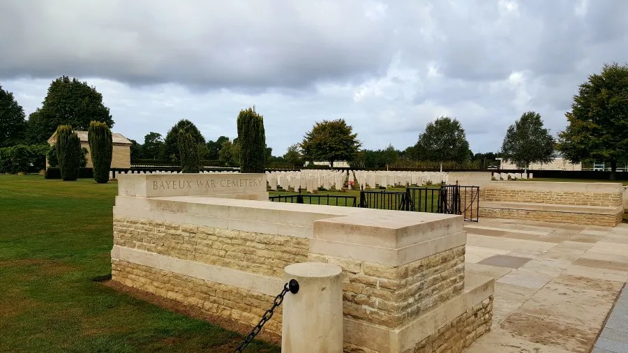 Das Bayeux War Cemetery mit gepflegten Rasenflächen und Grabsteinen unter einem bewölkten Himmel.