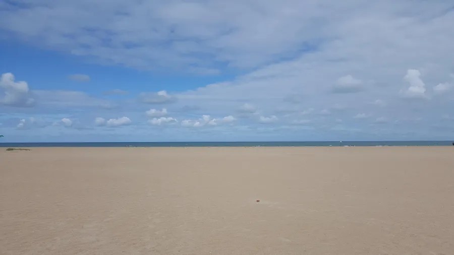 Weitläufiger Sandstrand mit sanften Wellen und bewölktem Himmel.
