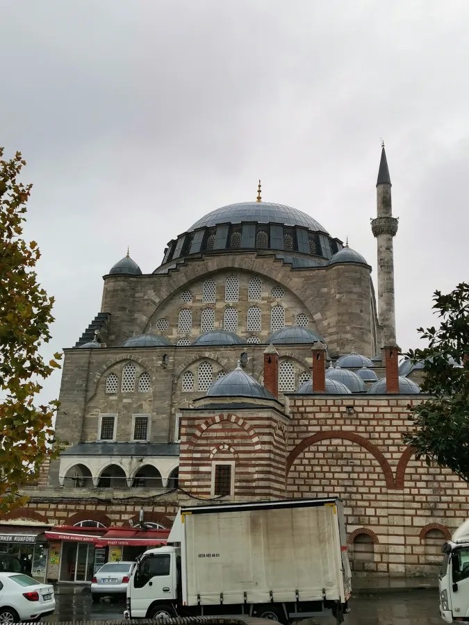 Blick auf die Mihrimah-Sultan-Moschee mit ihrer charakteristischen Kuppel und dem Minarett, umgeben von urbaner Architektur und Fahrzeugen.
