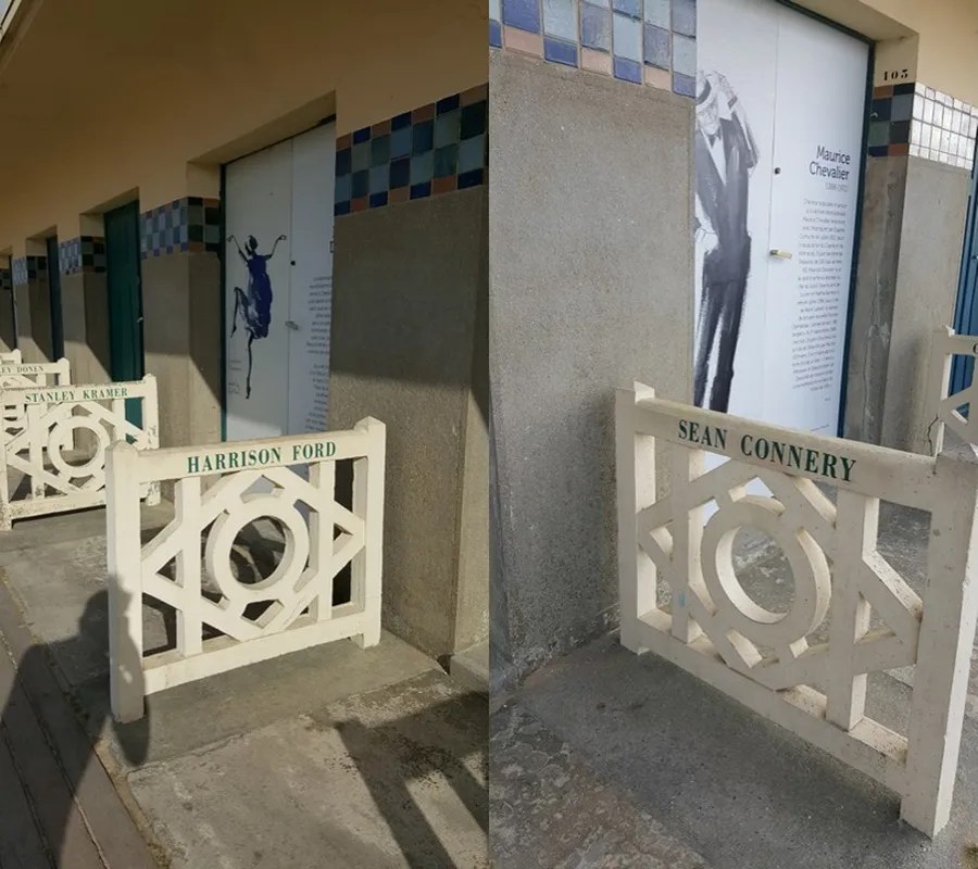 Zwei weiße Holzgeländer mit den Namen von berühmten Schauspielern, darunter Harrison Ford und Sean Connery, vor einem Gebäude mit Artistik-Grafik an der Wand.