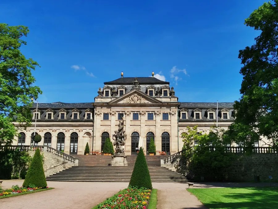 Das Fuldaer Stadtschloss, ein barockes Bauwerk, zeigt eine prächtige Fassade mit Stufen und Skulpturen vor einem klaren blauen Himmel.