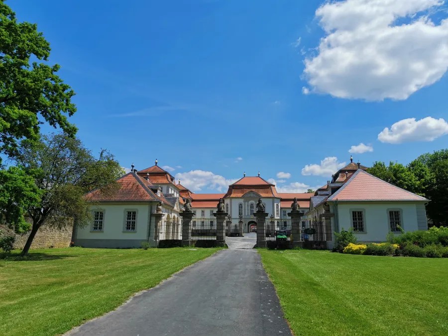 Das Schloss Fasanerie in Eichenzell, Hessen, umgeben von grünem Rasen und Bäumen, unter einem blauen Himmel mit weißen Wolken.