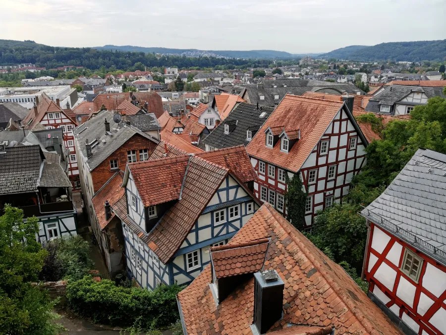 Blick auf die Dächer der historischen Altstadt von Marburg mit Fachwerkhäusern und einer hügeligen Landschaft im Hintergrund.