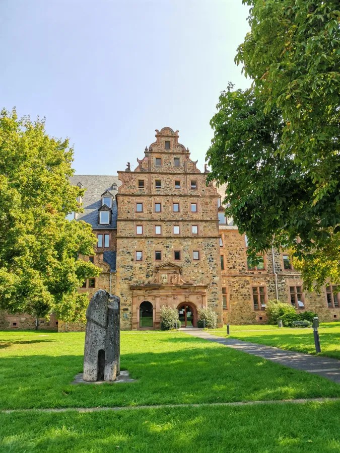 A historic building with a distinct architectural style, surrounded by greenery and a sculpture in the foreground.