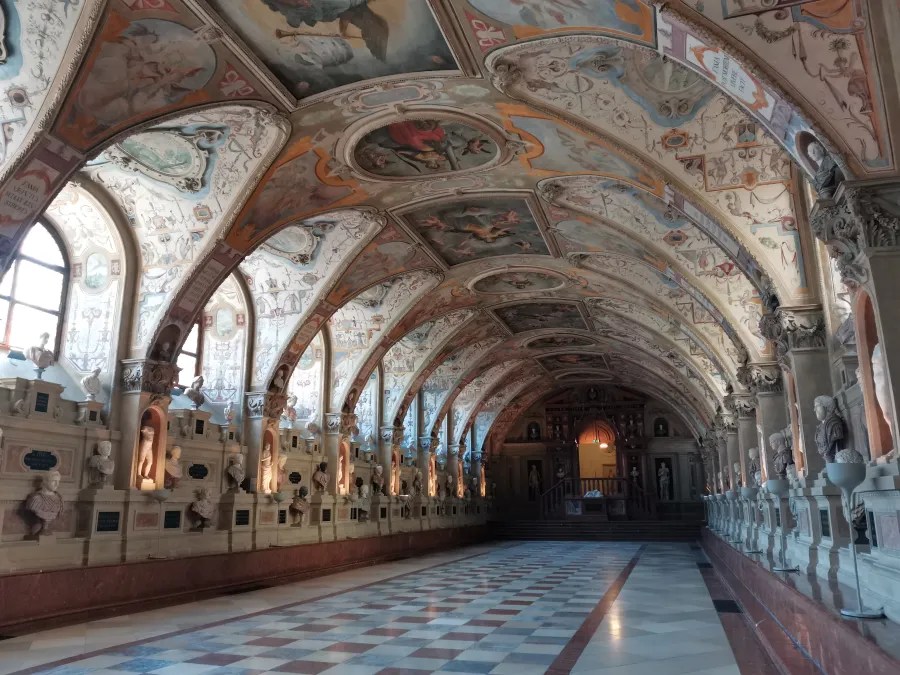 Der prunkvolle Innenraum eines historischen Raums mit kunstvollen Fresken an der Decke, beleuchtet von den Fenstern auf der linken Seite. An den Wänden stehen Skulpturen und Statuen, die in Nischen platziert sind.