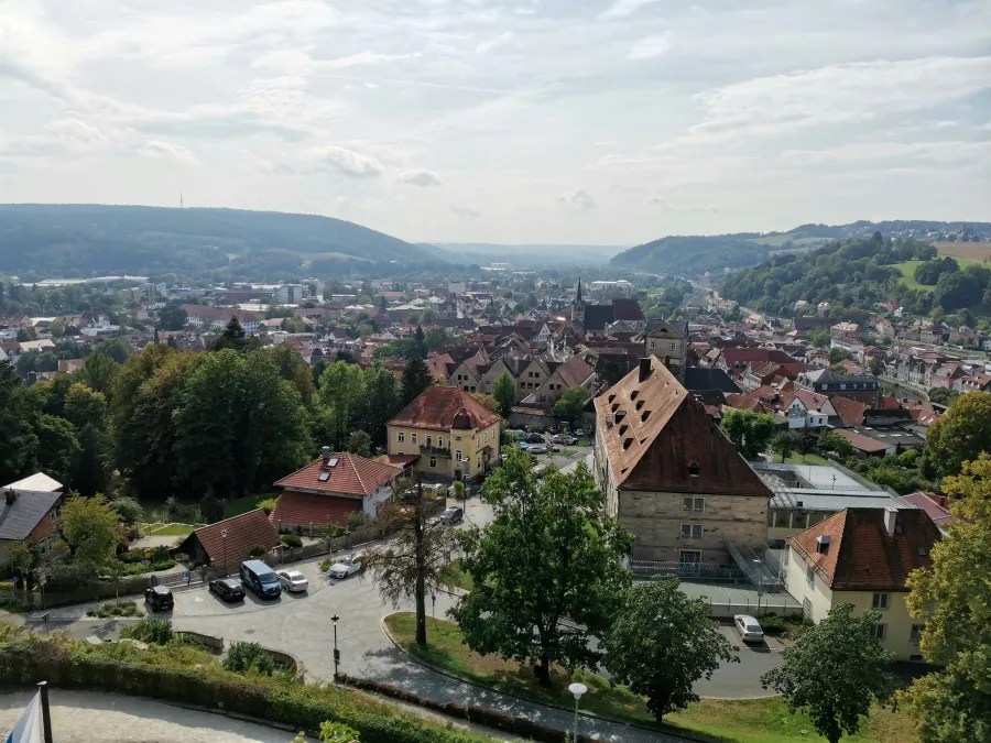 Panoramaansicht auf die Stadt Coburg mit grünen Hügeln im Hintergrund und historischen Gebäuden im Vordergrund. Der Himmel ist teilweise bewölkt.